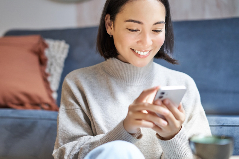 A woman is holding and looking at her phone, she is smiling.