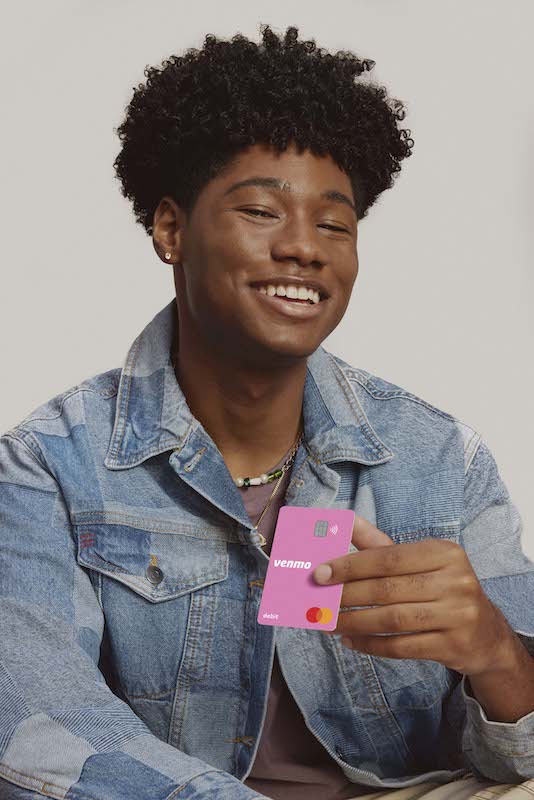 A young teen sits on a couch holding a pink Venmo card.